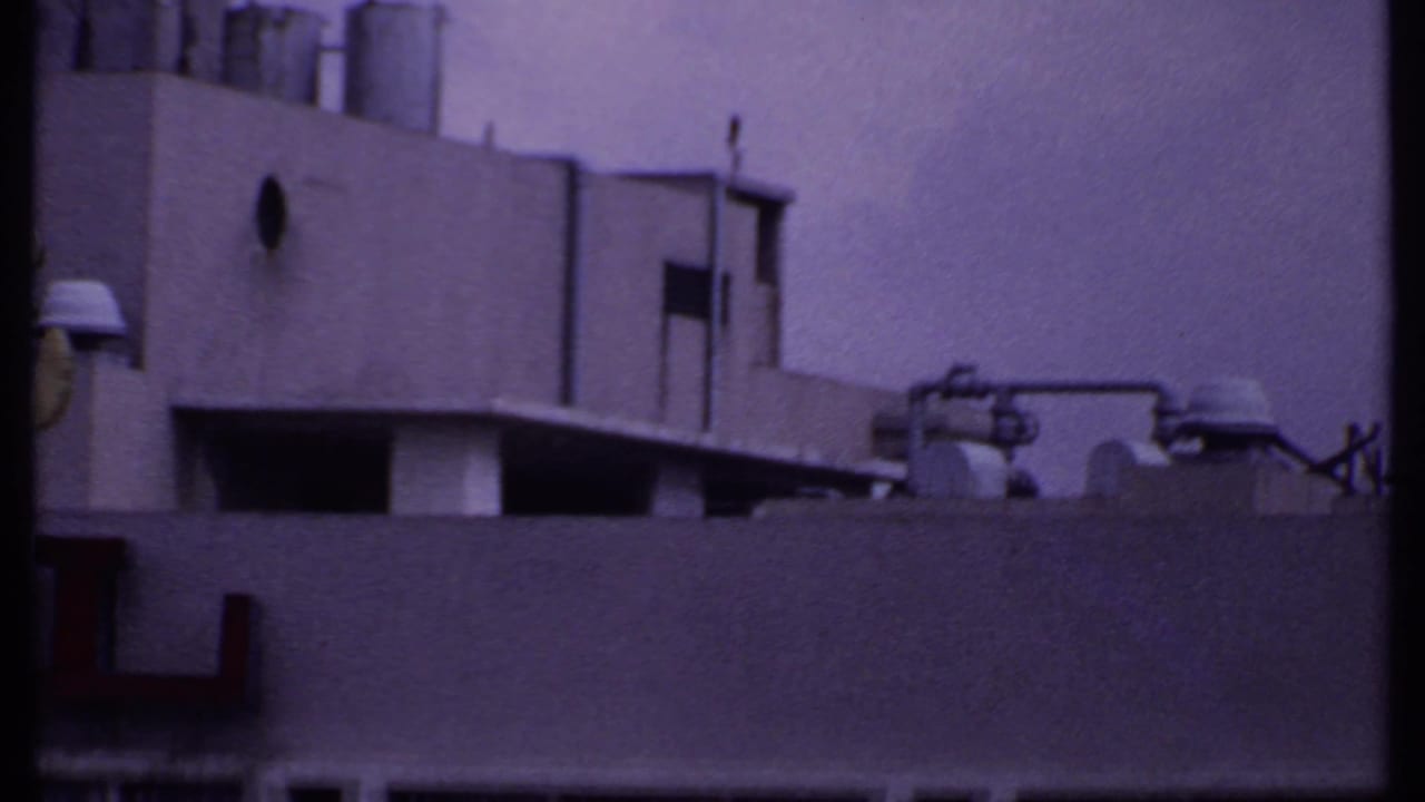 1969 India 8mm frame showing a cropped commercial building facade with partial red hotel lettering, vents, and rooftop equipment.