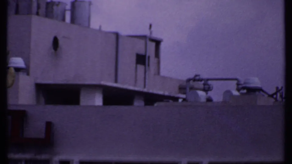 1969 India 8mm frame showing a cropped commercial building facade with partial red hotel lettering, vents, and rooftop equipment.