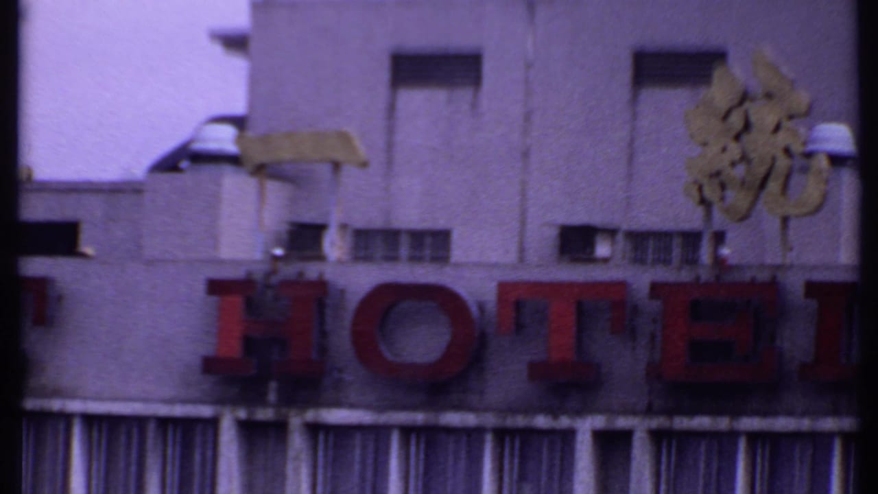 1969 India 8mm frame showing the hotel sign, gold characters, small vents, and striped awning fabric below the facade.