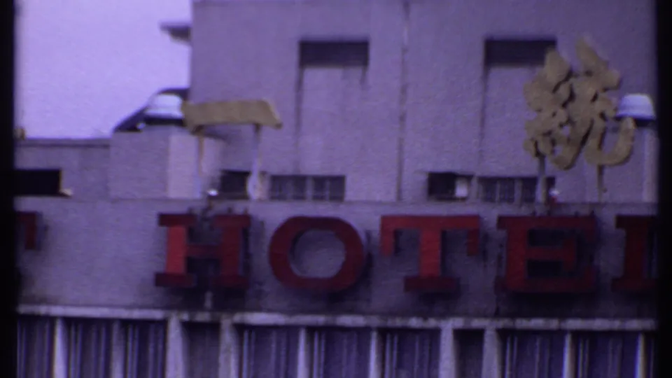 1969 India 8mm frame showing the hotel sign, gold characters, small vents, and striped awning fabric below the facade.