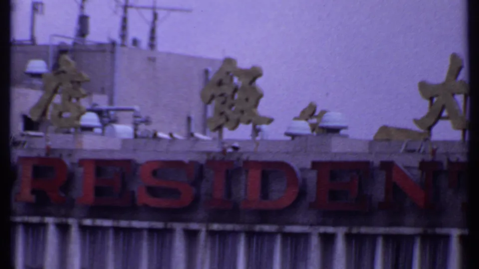 1969 India 8mm frame showing red RESIDENT lettering on a hotel facade, with Chinese characters above and vertical window slats below.