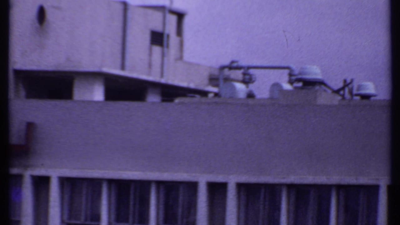 Upper portion of a flat-roofed building with rooftop vents and window bays.