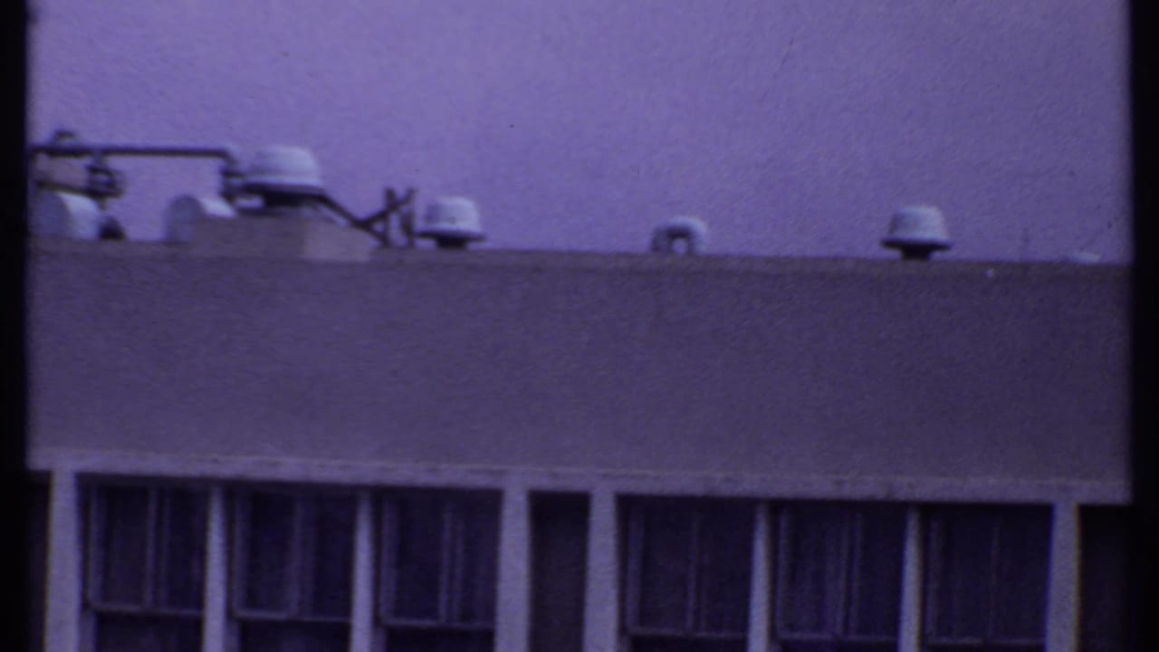 1969 India 8mm view of a building roofline with multiple vent caps, a broad parapet, and dark vertical window openings below.