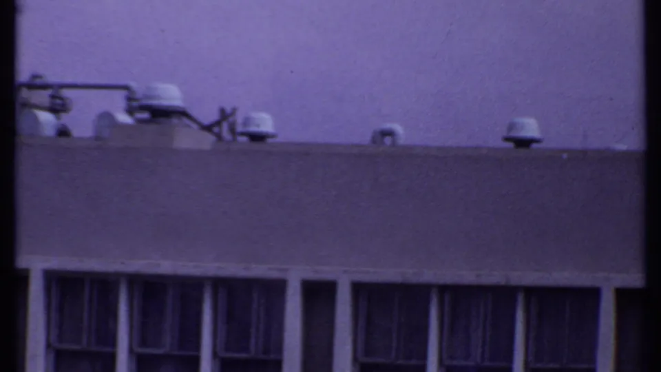 1969 India 8mm view of a building roofline with multiple vent caps, a broad parapet, and dark vertical window openings below.