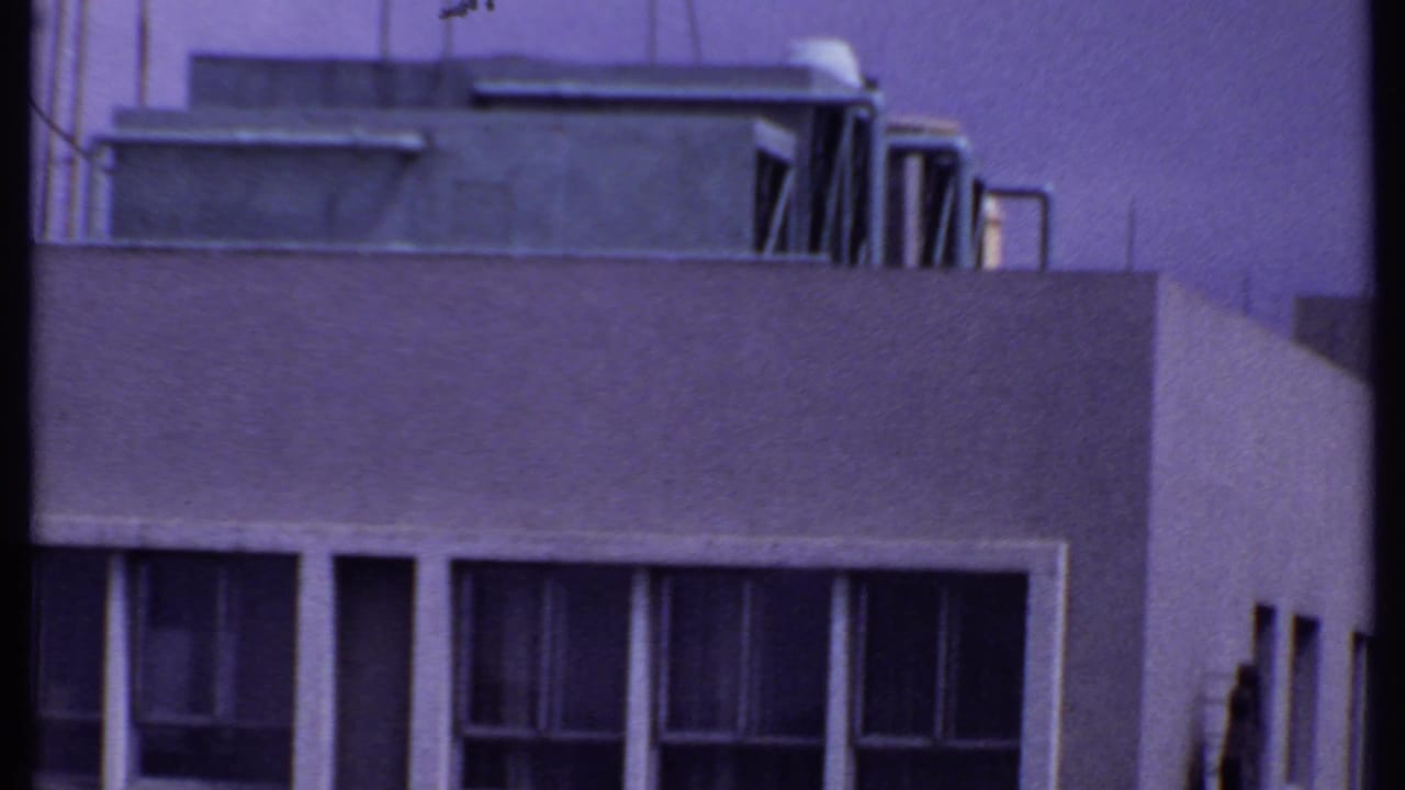 1969 India 8mm view of a building corner, showing rooftop mechanical housing, parapet walls, vents, and repeated vertical windows.