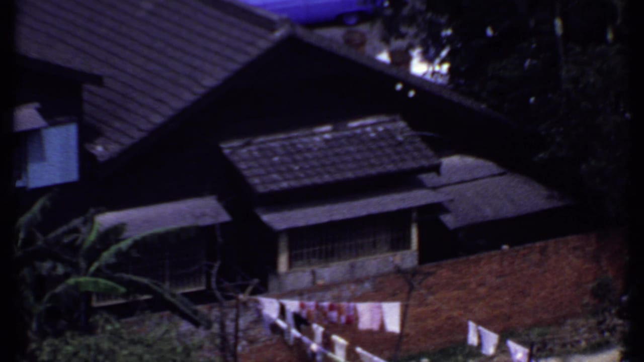 1969 India aerial home-movie frame showing dark tiled roofs, exterior walls, trees, and laundry seen from above.