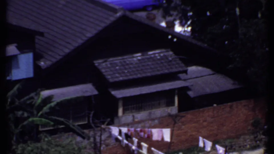 1969 India aerial home-movie frame showing dark tiled roofs, exterior walls, trees, and laundry seen from above.