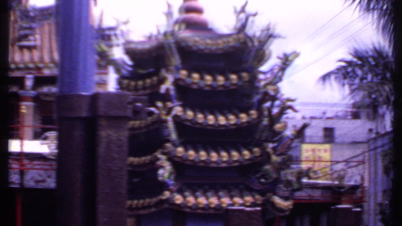 1969 India home-movie frame showing an ornate Chinese-style temple facade with upturned roof tiers, red railings, and foreground columns.