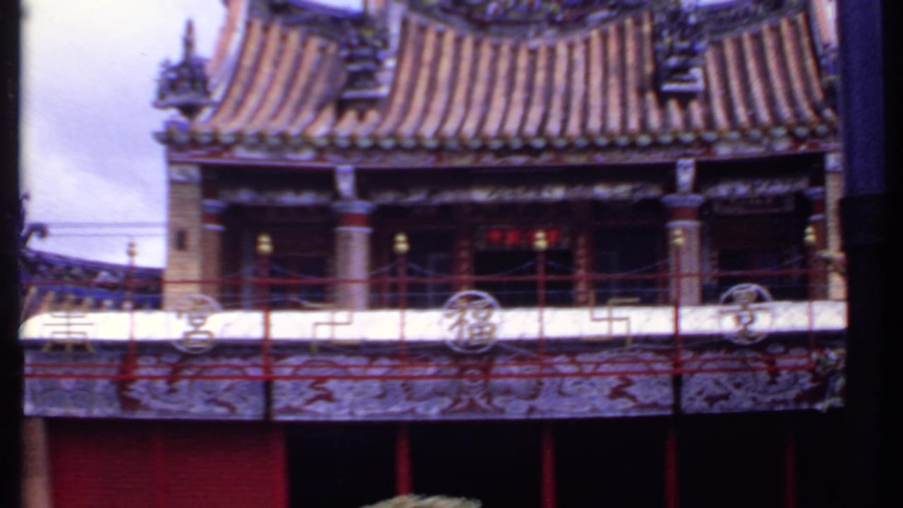 1969 India home-movie view of temple balcony architecture, with red railings, painted panels, columns, and a layered tile roof.