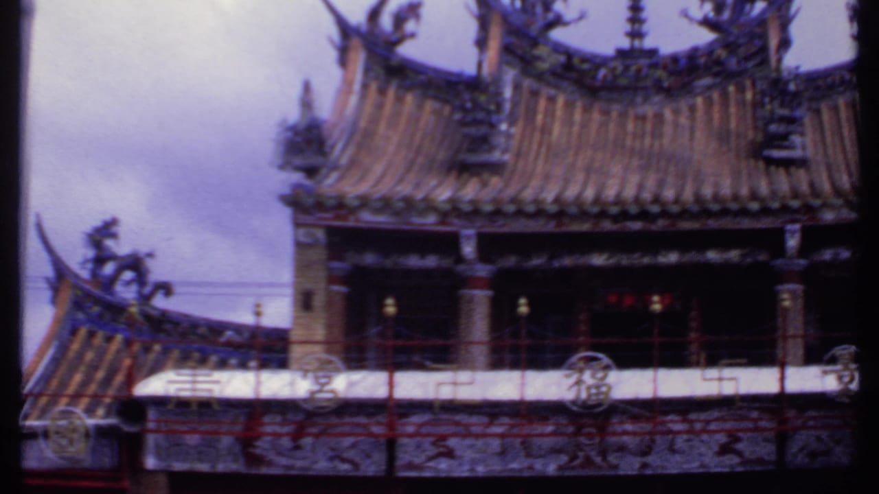 Ornate temple roof with curved ridges and dragon-like sculptures beside a white building.