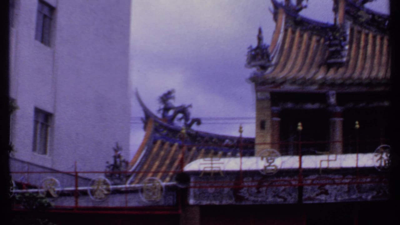 Upper portion of a Chinese-style temple with tiled roof ornaments, red railing, and adjacent white multi-story building in 1969 India-listed footage.