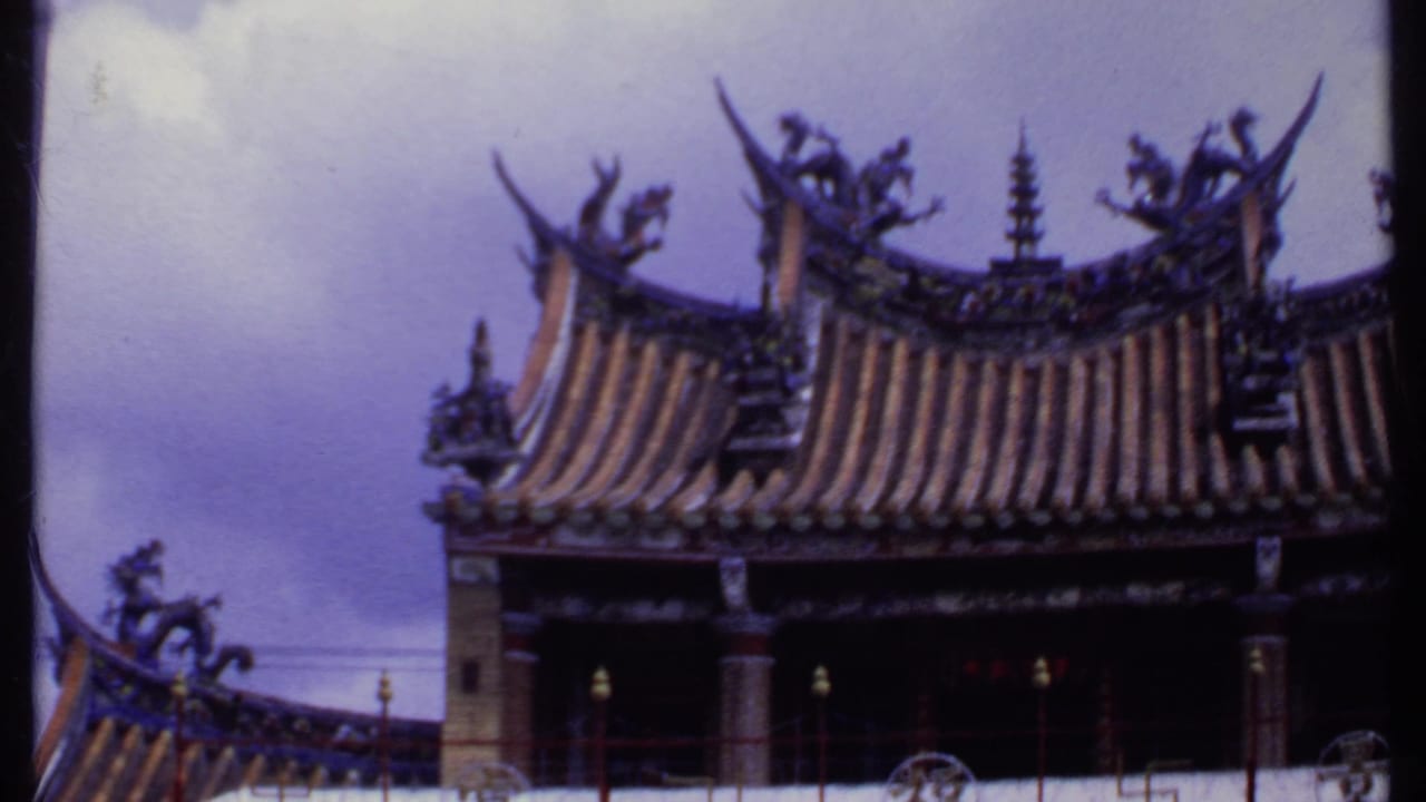 1969 India-labeled 8mm still showing a closer view of a temple roof, curved tile rows, carved roof figures, red railing, and pale sky.