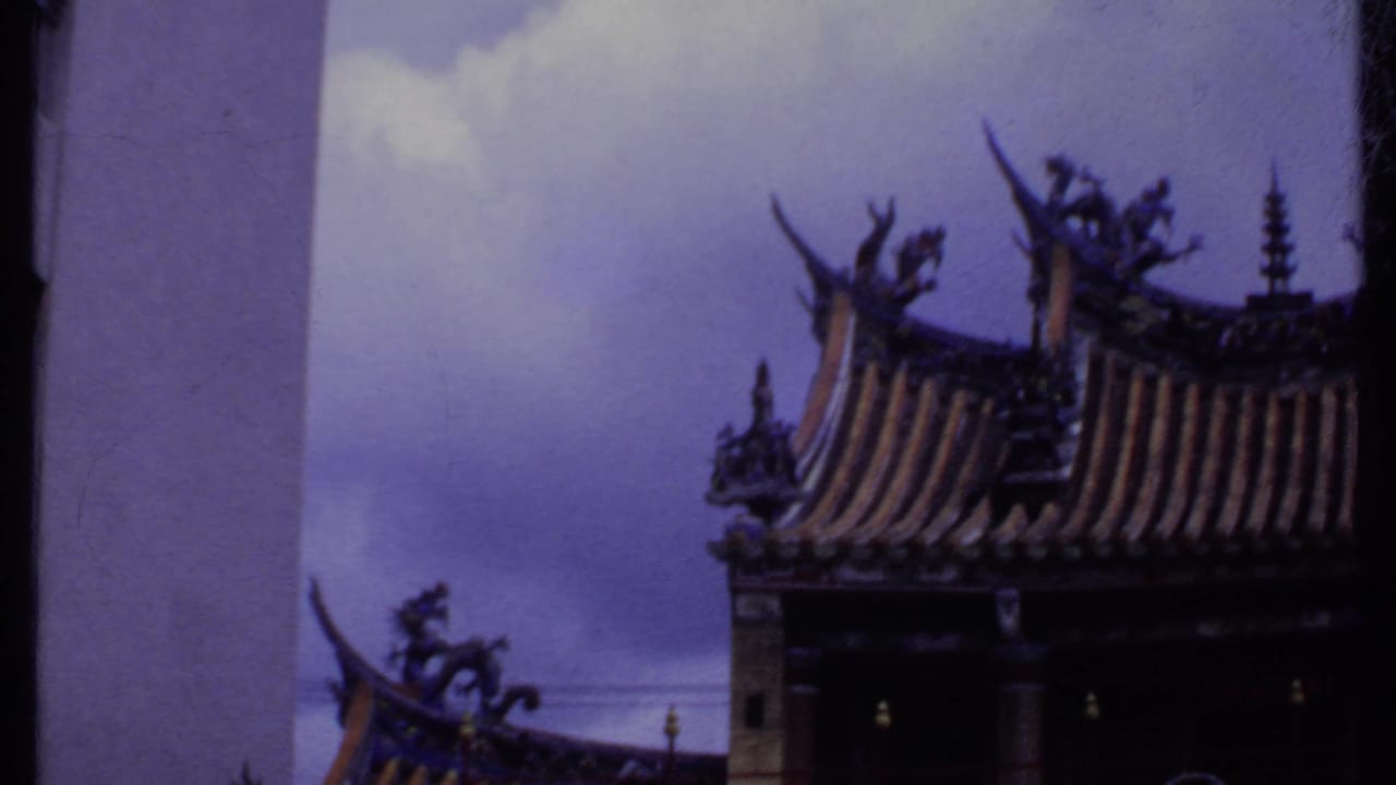 Ornate upturned roofline beside a white multi-story building under a cloudy sky.