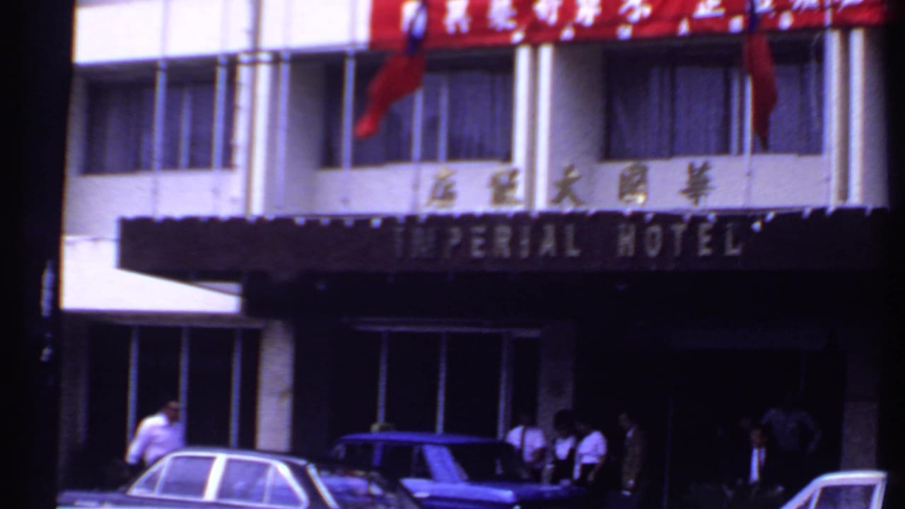 Hotel entrance with Imperial Hotel canopy, Chinese characters, pedestrians, and cars at curbside.