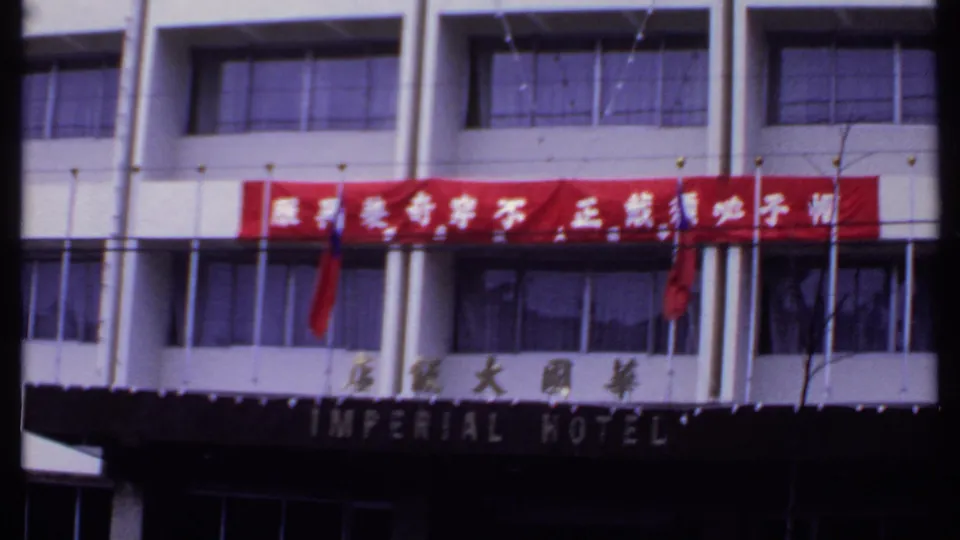 Street-level 8mm view of the Imperial Hotel in India with Chinese lettering, red banner, white facade, and dark entrance canopy.
