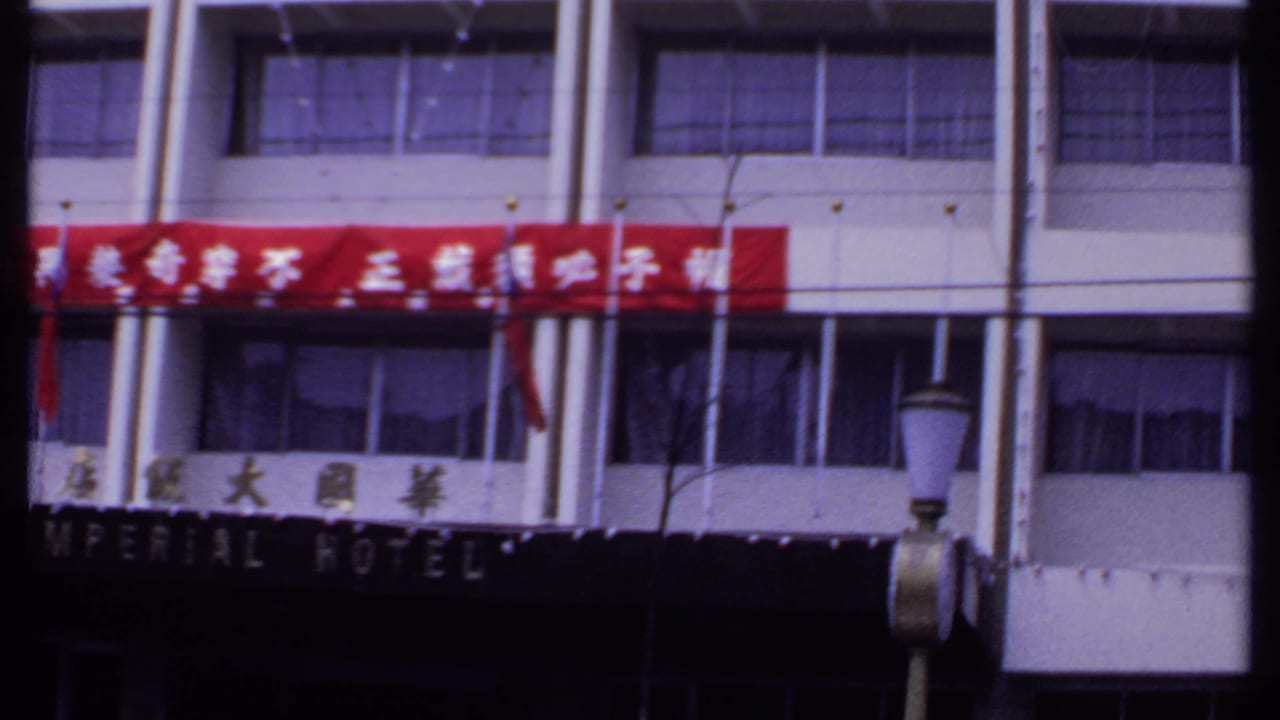 Final 8mm frame of the Imperial Hotel exterior in India, showing the red banner, Chinese and English signage, windows, flags, and streetlamp.