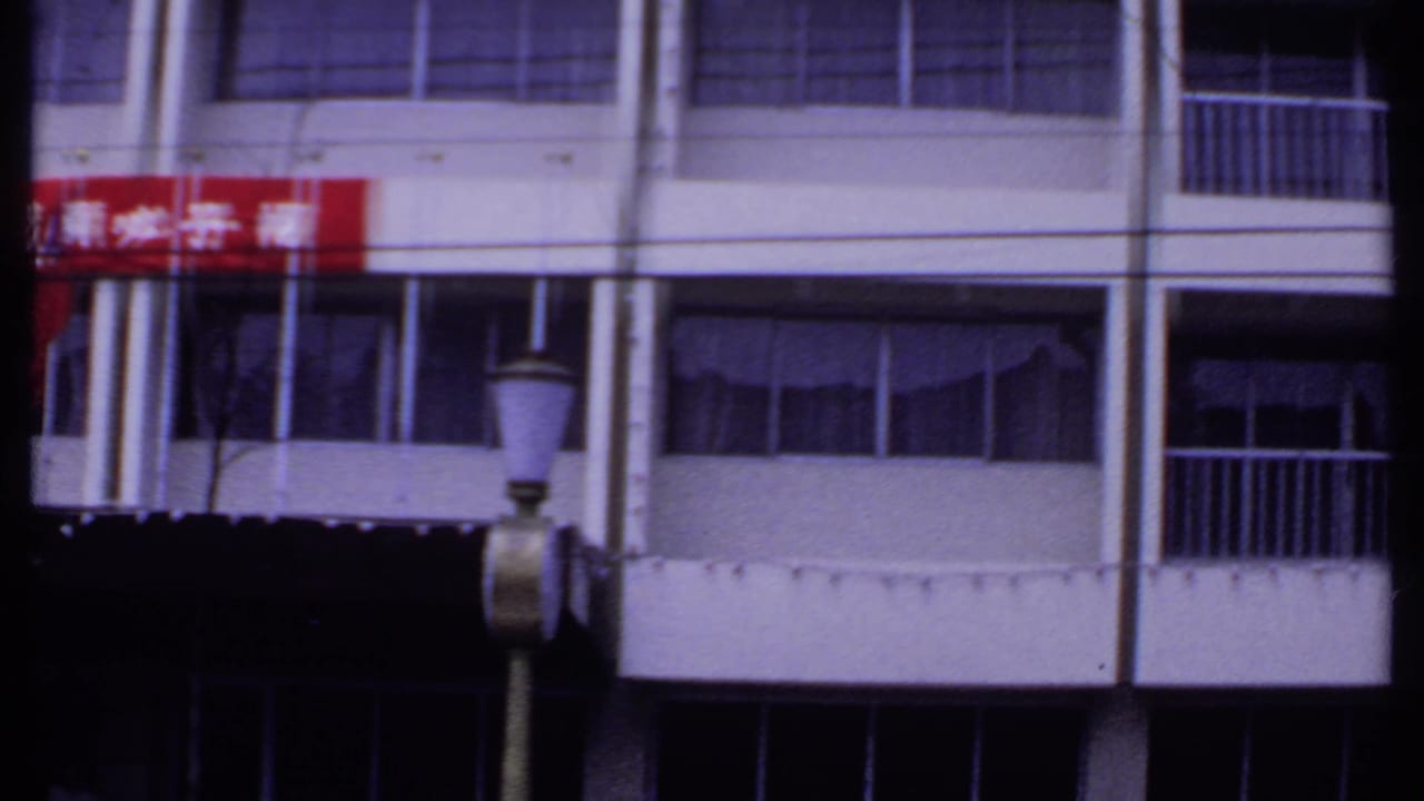 Upper building facade with balcony railings, windows, red banner fragment, and street lamp.