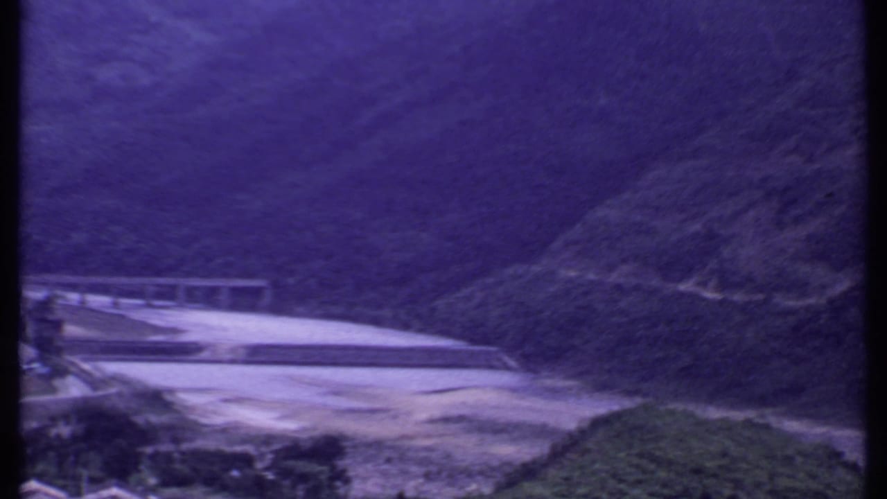1969 India 8mm view of a mountain river valley with a pale dam or bridge and dark green slopes in the background.