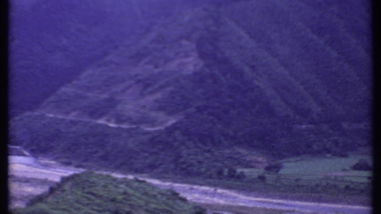 1969 India 8mm frame showing a steep mountain slope, river channel, valley vegetation, and aged purple film color.
