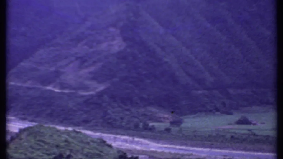 1969 India 8mm frame showing a pale road curving through a green valley below dark, forested hills and a purple color cast.