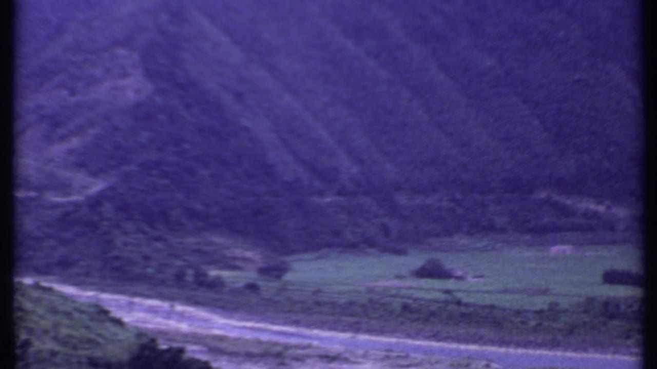 Curving valley road with green fields and wooded hills beyond.