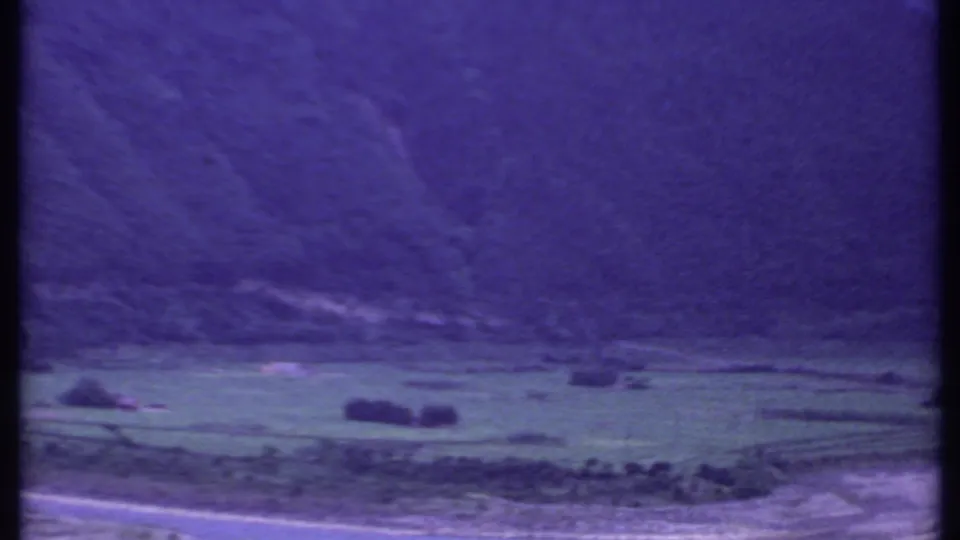 Final 1969 India 8mm frame holding on green fields, a foreground road, scattered trees, and a dark hillside under strong color drift.