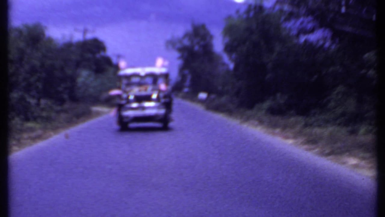 Jeep-style vehicle approaching on a paved road bordered by trees.