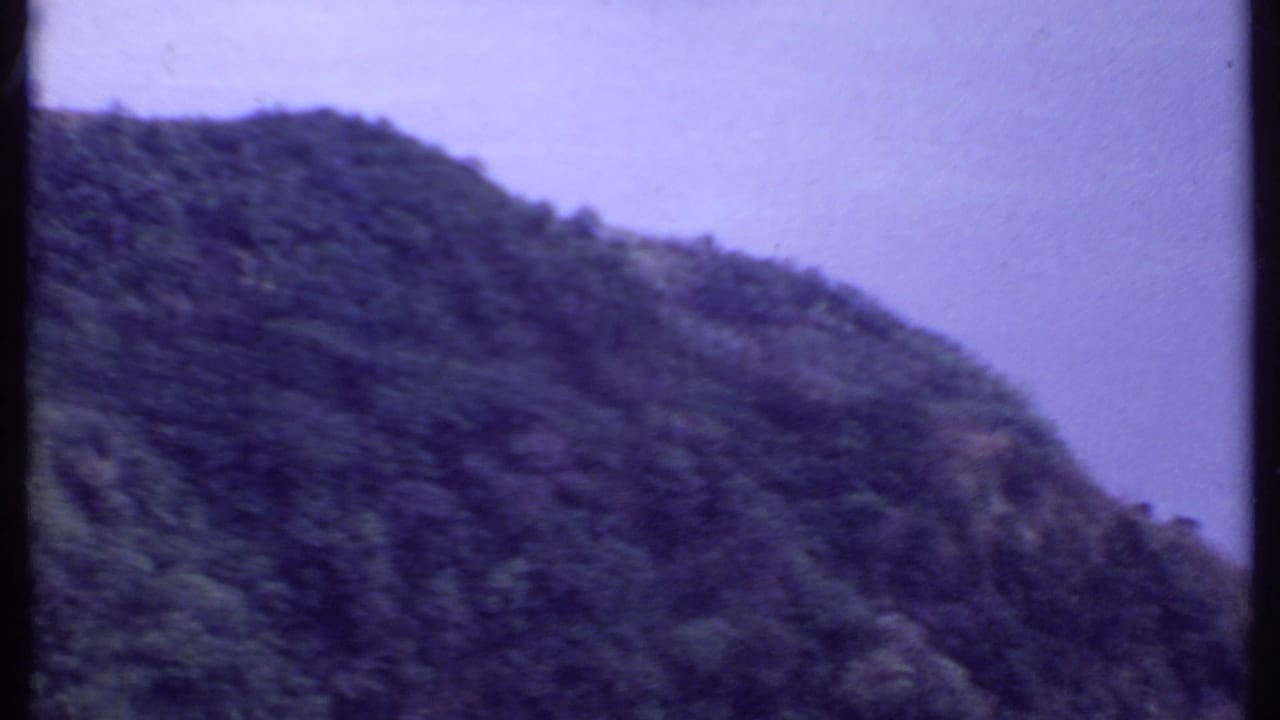 1969 India 8mm frame with a dark green forested mountain slope under a pale, hazy sky.