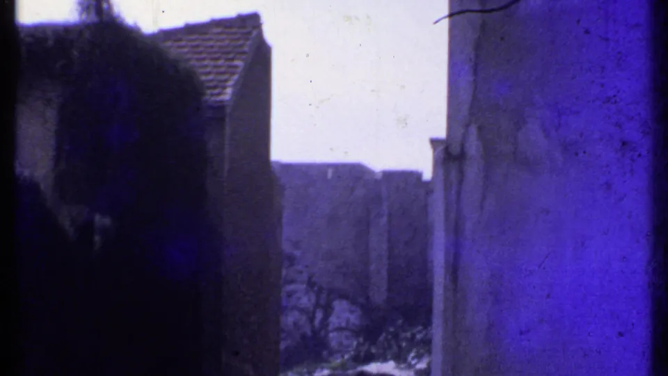 1969 Kenya home-movie frame showing pale urban buildings, tiled roofs, and dark window framing with a purple-blue film cast.