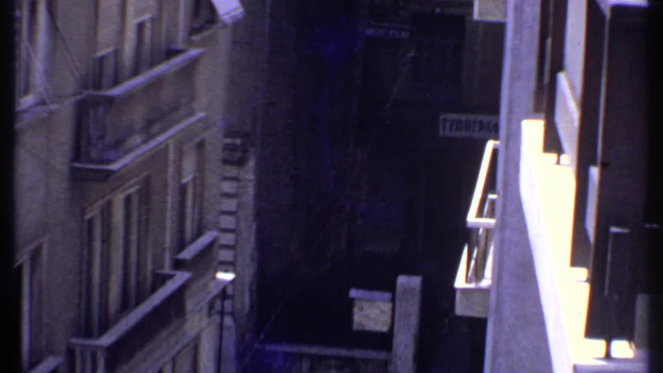 1969 Kenya home-movie view of weathered concrete apartments, stacked balconies, and a dark recessed passage between buildings.