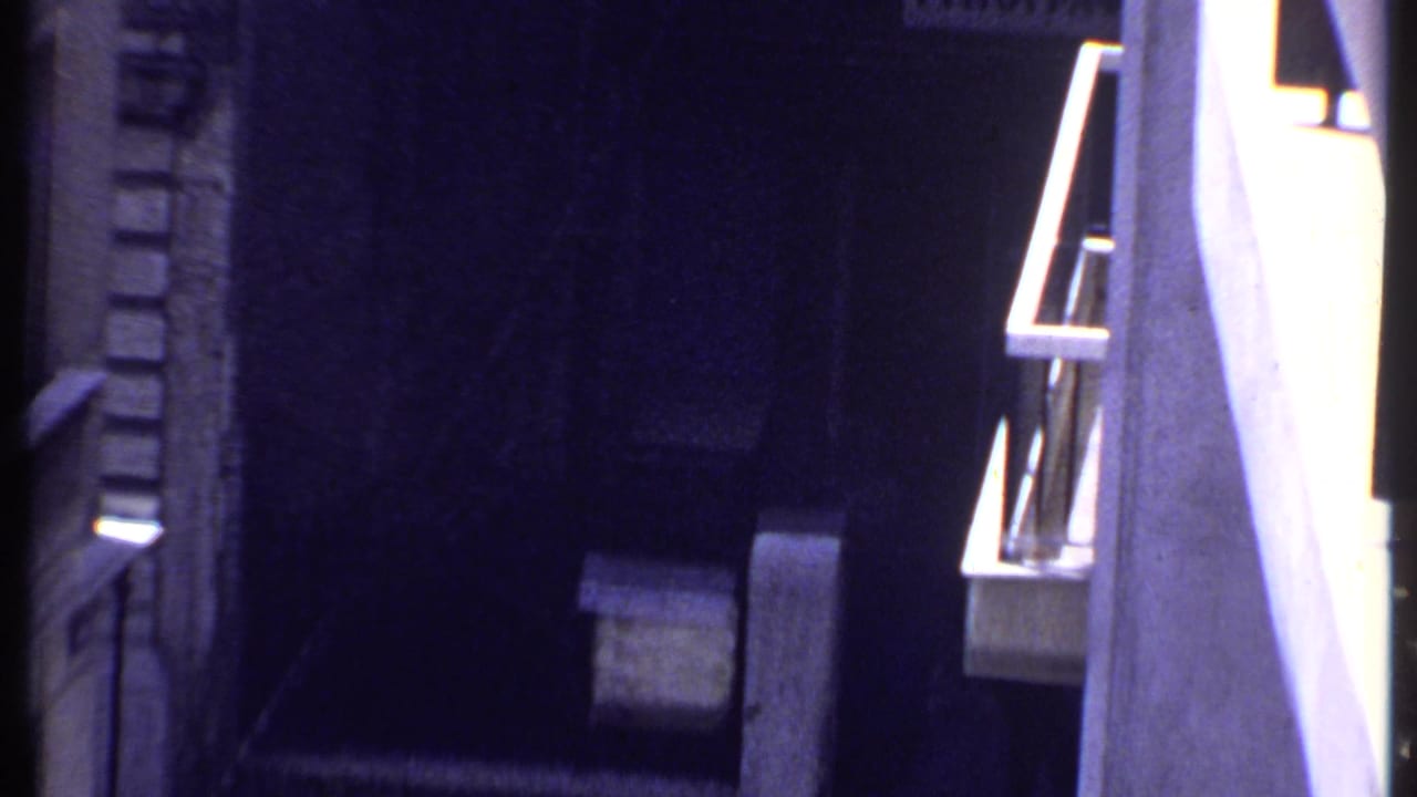 1969 Kenya 8mm frame showing a pale van parked in deep shadow between exterior building walls.