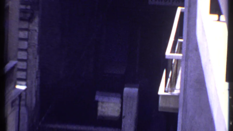 1969 Kenya 8mm frame showing a pale van parked in deep shadow between exterior building walls.
