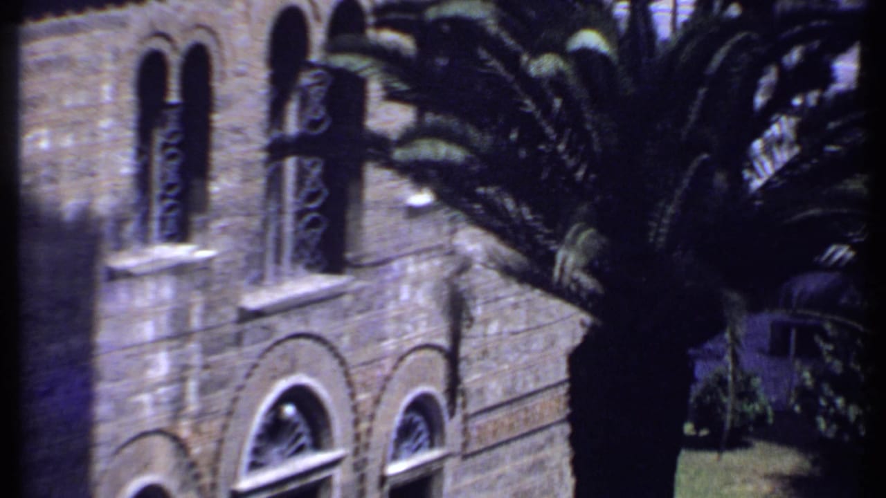 1969 Kenya 8mm frame showing a stone church-like facade, arched windows, and a palm tree partly blocking the view.
