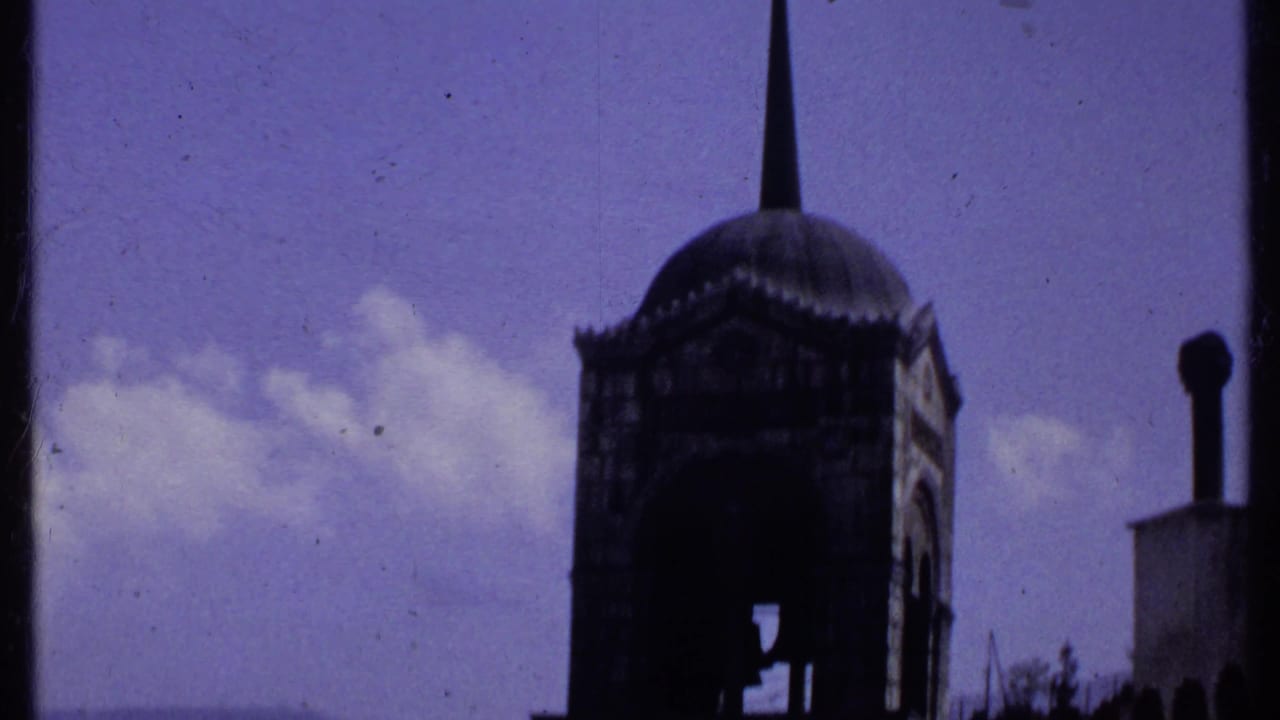 Domed tower with pointed spire silhouetted against blue sky and clouds.
