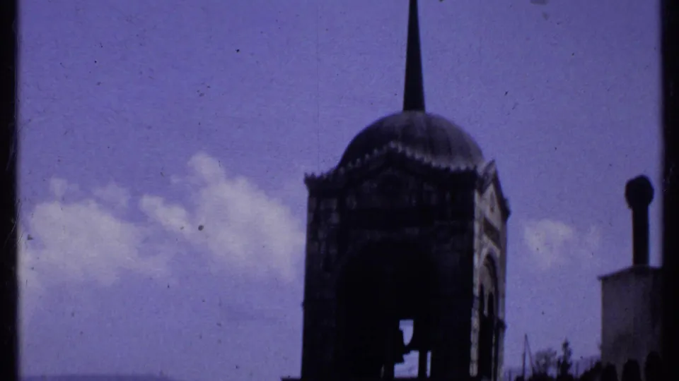 1969 Kenya 8mm frame showing a dark domed church tower and tall spire against blue sky with distant clouds.