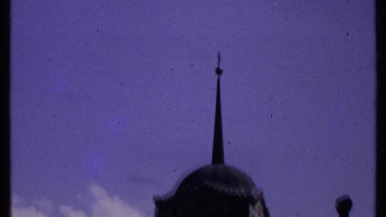 Pointed spire and part of a domed tower under a blue sky.
