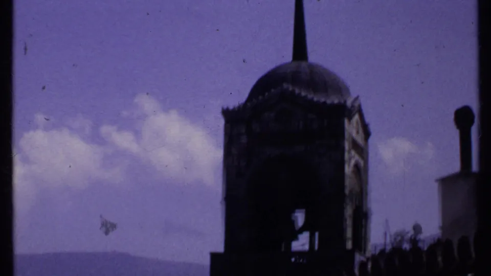 1969 Kenya 8mm frame showing the domed tower and spire with clouds, trees, and a faint mountain ridge beyond.
