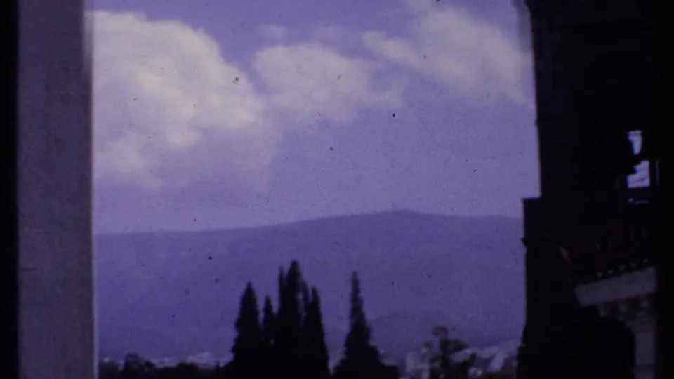 1969 Kenya travel frame with a mountain ridge, bright clouds, trees, and the cropped edge of the church tower.