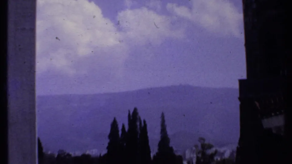 1969 Kenya 8mm frame with silhouetted trees and a dark vertical edge in front of hazy mountains under a purple-blue sky.