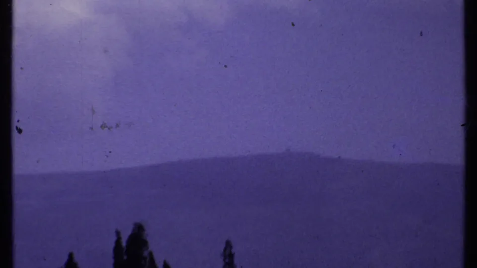 1969 Kenya 8mm frame showing a dark central vertical form over distant mountains, blue haze, and low tree silhouettes.