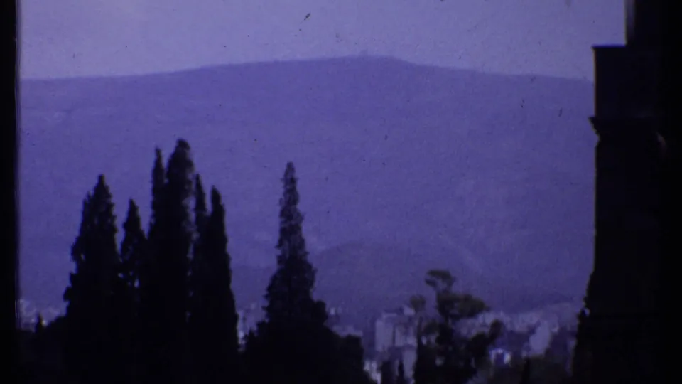 1969 Kenya 8mm frame showing tall dark trees, distant hazy mountains, faint valley structures, and a dark frame edge at right.