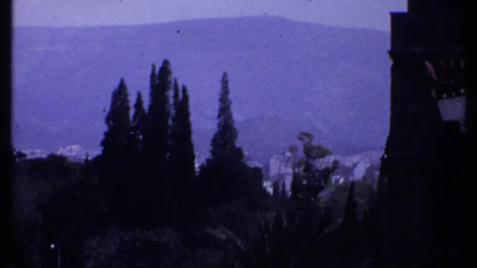 1969 Kenya home-movie frame looking past balcony columns toward cypress-like trees and hazy distant hills.