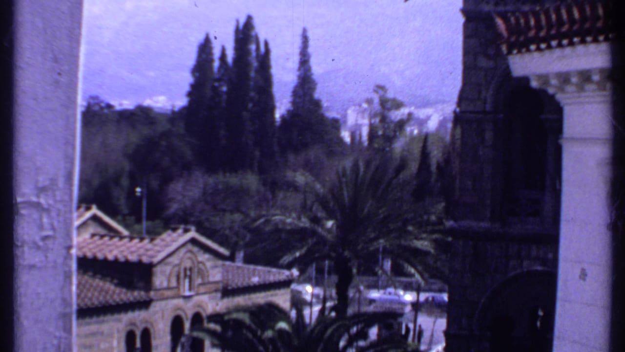 Stone church building with tiled roof, palms, trees, and balcony columns.