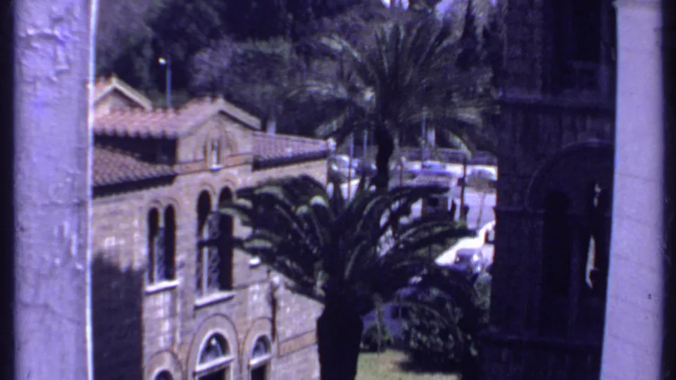 1969 Kenya frame showing the church facade below, with arched windows, tiled roof, and a large palm beside it.