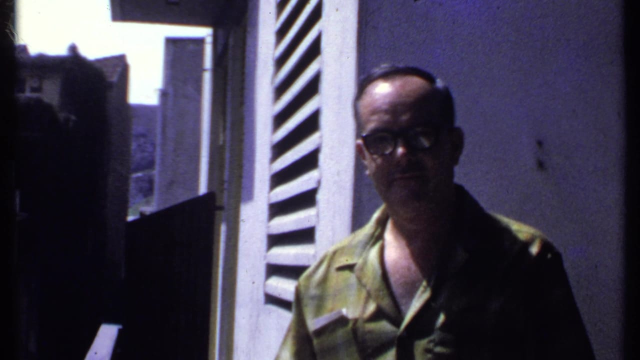 Man in glasses stands beside a white louvered shutter and open doorway.