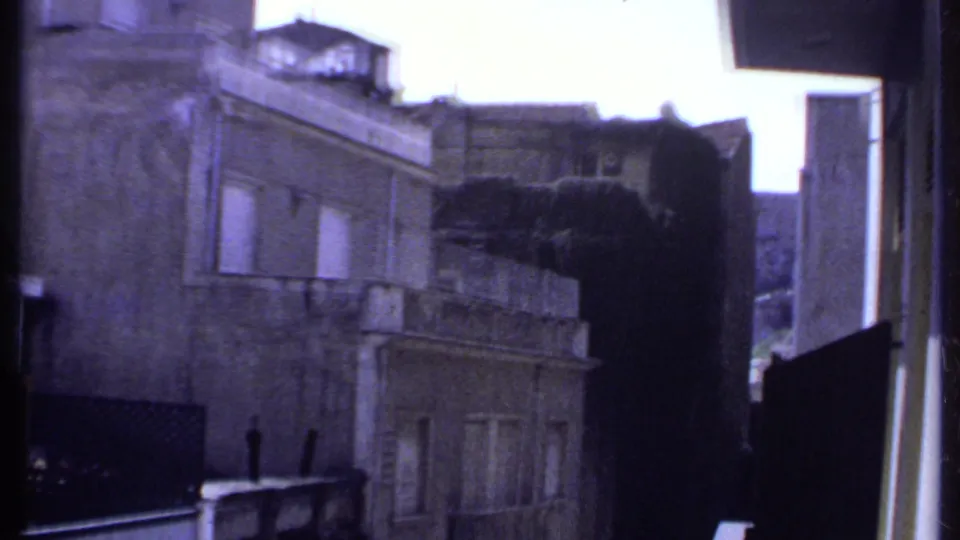 A 1969 Kenya city view shows weathered facades, shuttered windows, and nearby rooftops filmed from a balcony.
