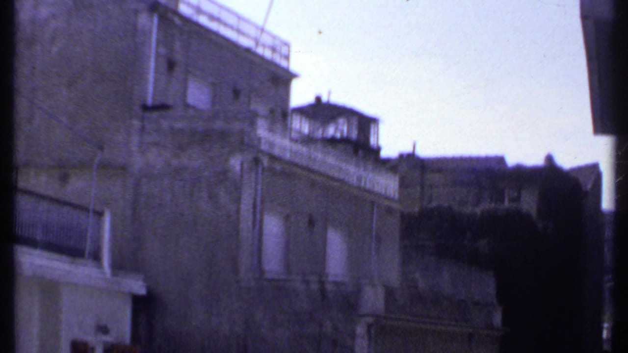 1969 Kenya 8mm frame showing a weathered exterior building facade, balcony railings, shuttered windows, and roofline details.