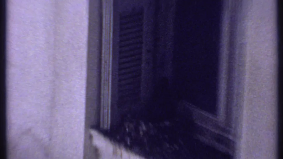 1969 Kenya 8mm frame looking past a nearby wall and dark shutter toward adjacent weathered building surfaces.