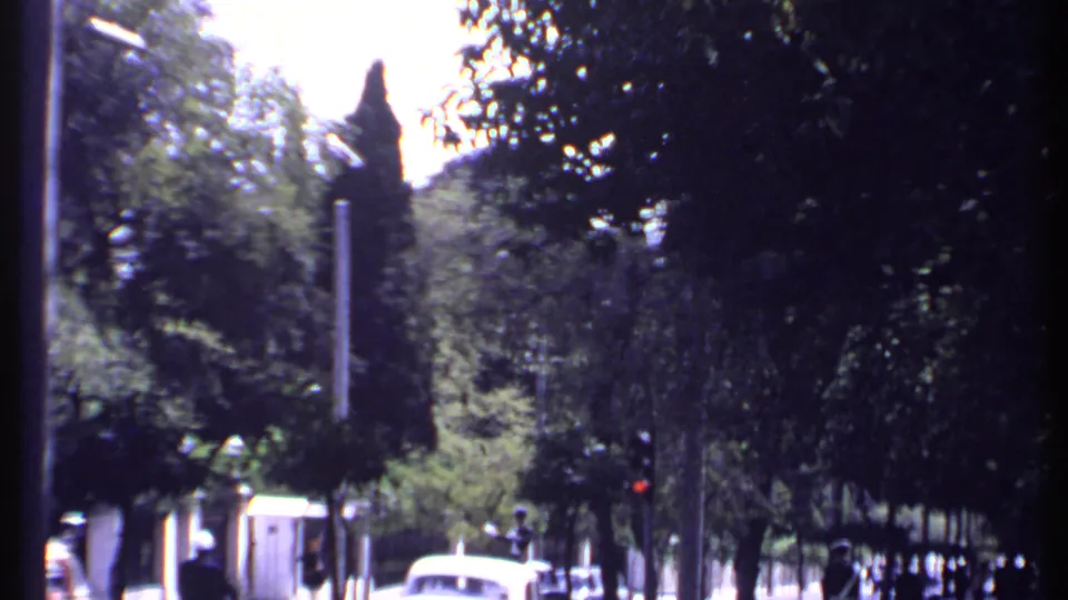 1969 Kenya city street frame showing cars and distant pedestrians beneath trees, with soft 8mm color and grain.