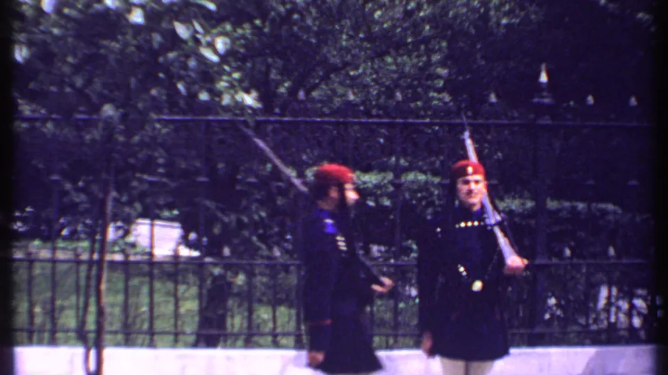 Two guards in dark uniforms and red hats appear to exchange positions in this 1969 Kenya home-movie frame.